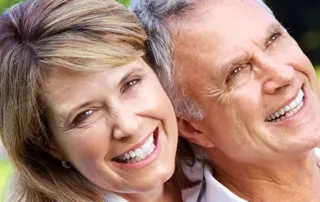 A smiling older couple stands close together outdoors, both wearing white shirts. The woman leans her head on the man’s shoulder as they enjoy the bright day, their cheerful expressions showing no signs of ADHD symptoms. Lush green foliage blurs in the background. - The Parker Group A smiling older couple stands close together outdoors, both wearing white shirts. The woman leans her head on the man’s shoulder as they enjoy the bright day, their cheerful expressions showing no signs of ADHD symptoms. Lush green foliage blurs in the background.