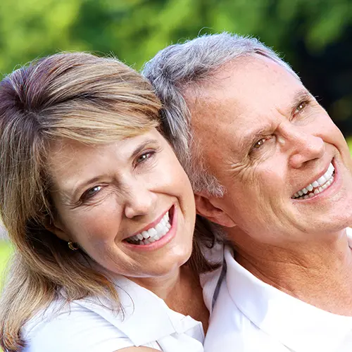 A smiling older couple stands close together outdoors, both wearing white shirts. The woman leans her head on the man’s shoulder as they enjoy the bright day, their cheerful expressions showing no signs of ADHD symptoms. Lush green foliage blurs in the background. A smiling older couple stands close together outdoors, both wearing white shirts. The woman leans her head on the man’s shoulder as they enjoy the bright day, their cheerful expressions showing no signs of ADHD symptoms. Lush green foliage blurs in the background.